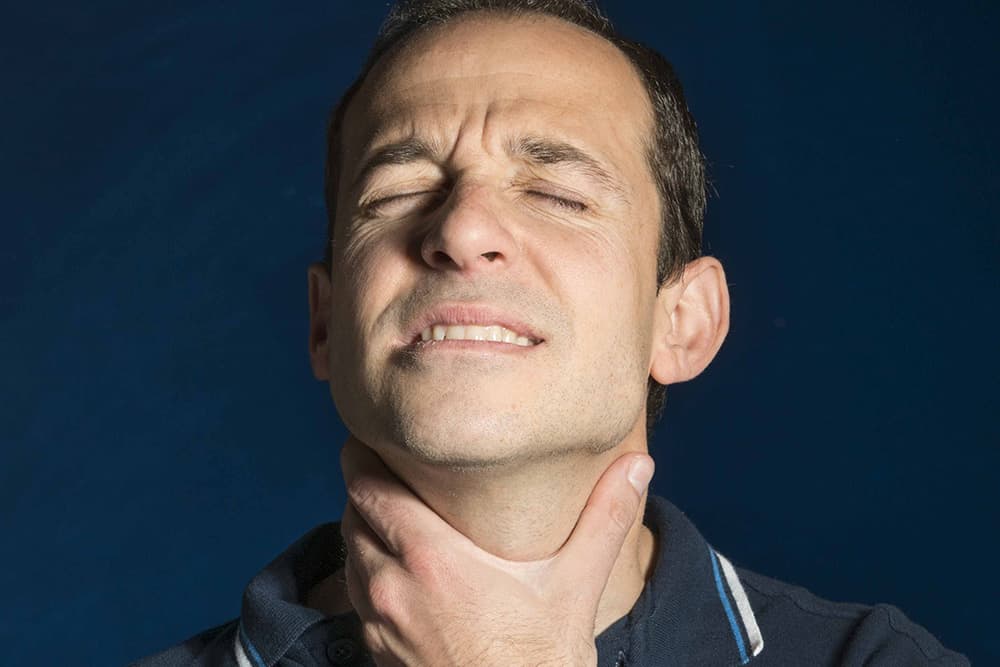 Mann mit starken Halsschmerzen fasst sich an den Hals
