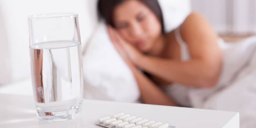 Frau liegt im Bett und schläft - Im Vordergrund ein Glas Wasser und Tabletten