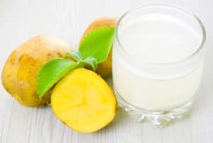 Glas mit Kartoffelsaft neben drei Kartoffeln