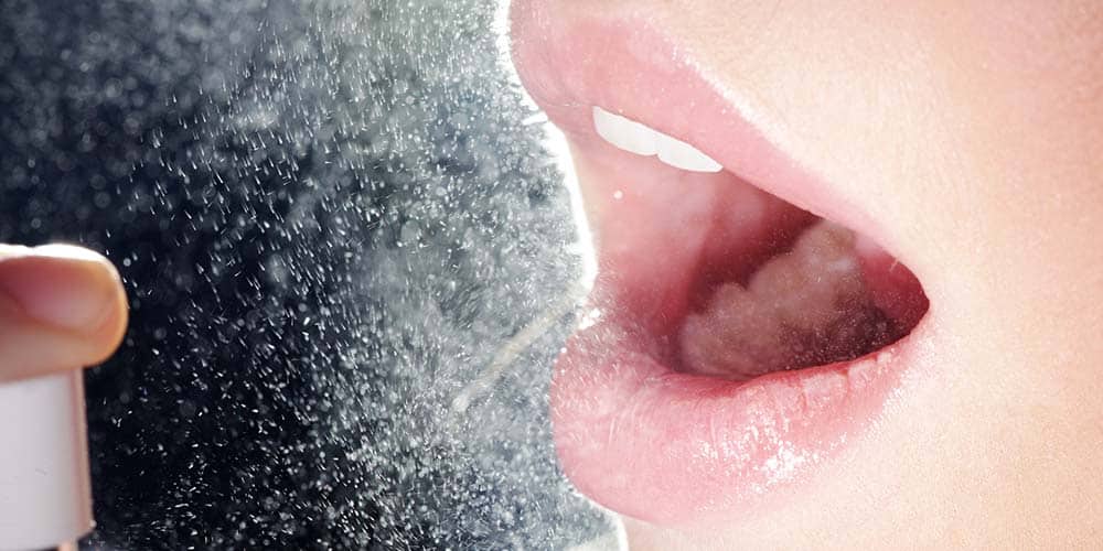 Frau sprüh sich Spray gegen Mundgeruch in den Mund
