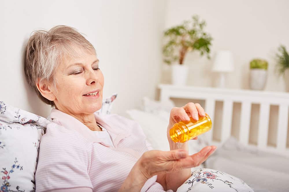 Ältere Frau nimmt Tabletten im Bett ein