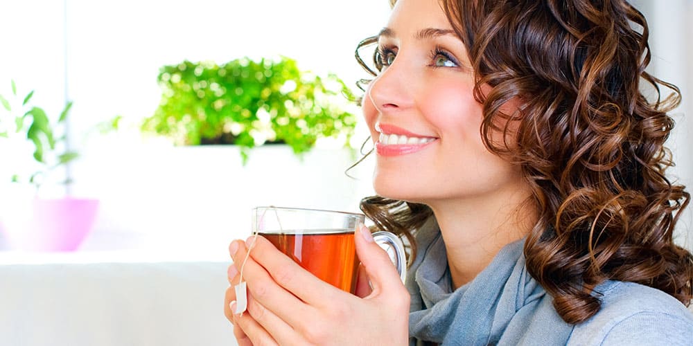 Frau trinkt ein Glas Tee und lächelt