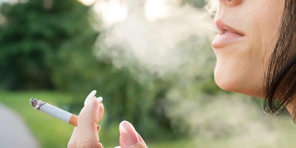 Frau hält Zigarette in der Hand und atmet Rauch aus