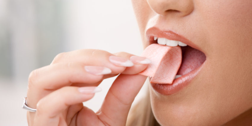 Closeup detail of woman putting pink chewing gum into her mouth.